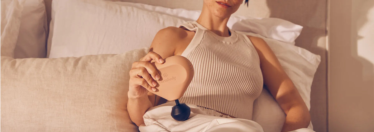 Eine Frau liegt im Bett und massiert ihren rechten Oberschenkel mit einer Theragun Mini Massagepistole