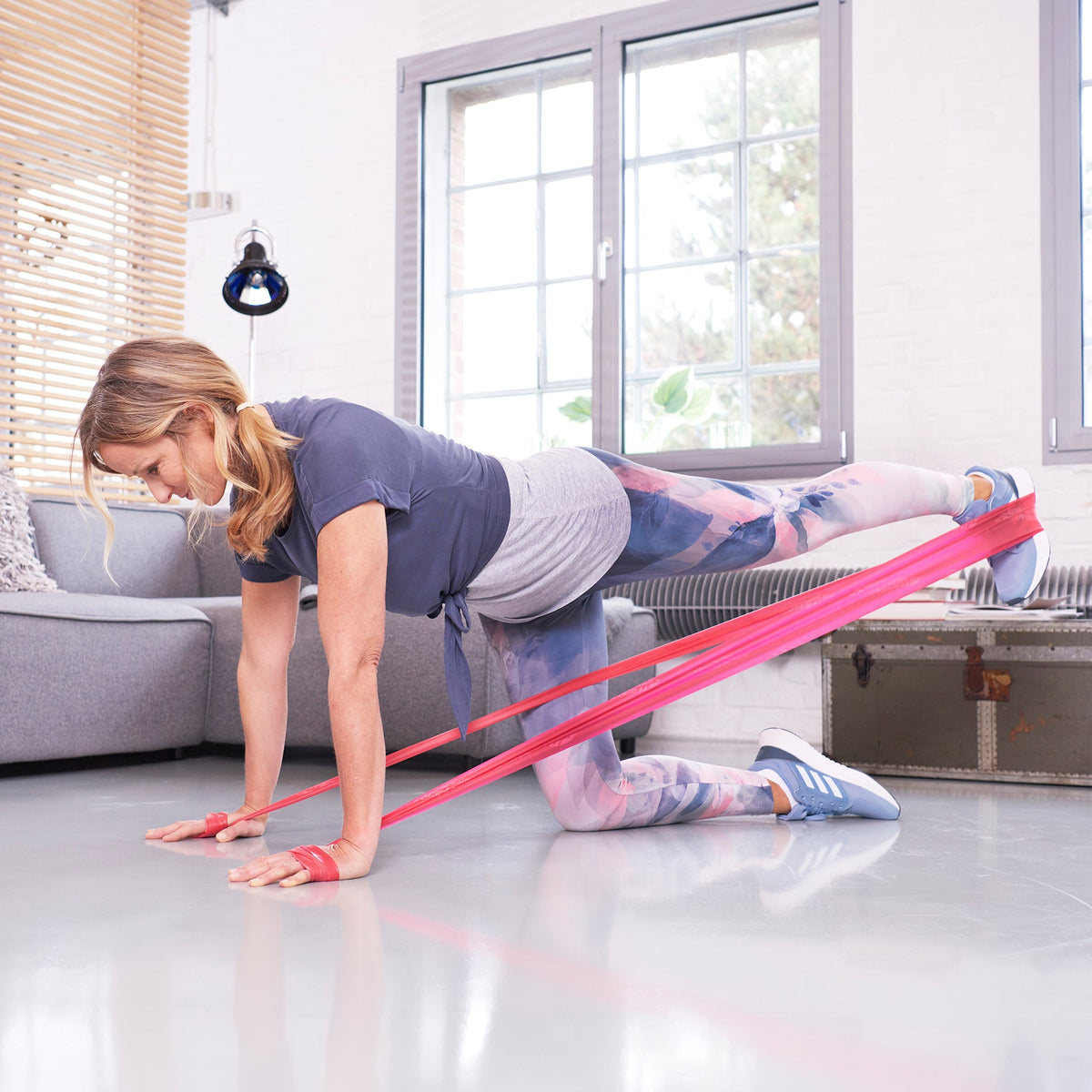 Sportlerin trainiert im Liegestütz ihr linkes Bein mit einem roten TheraBand