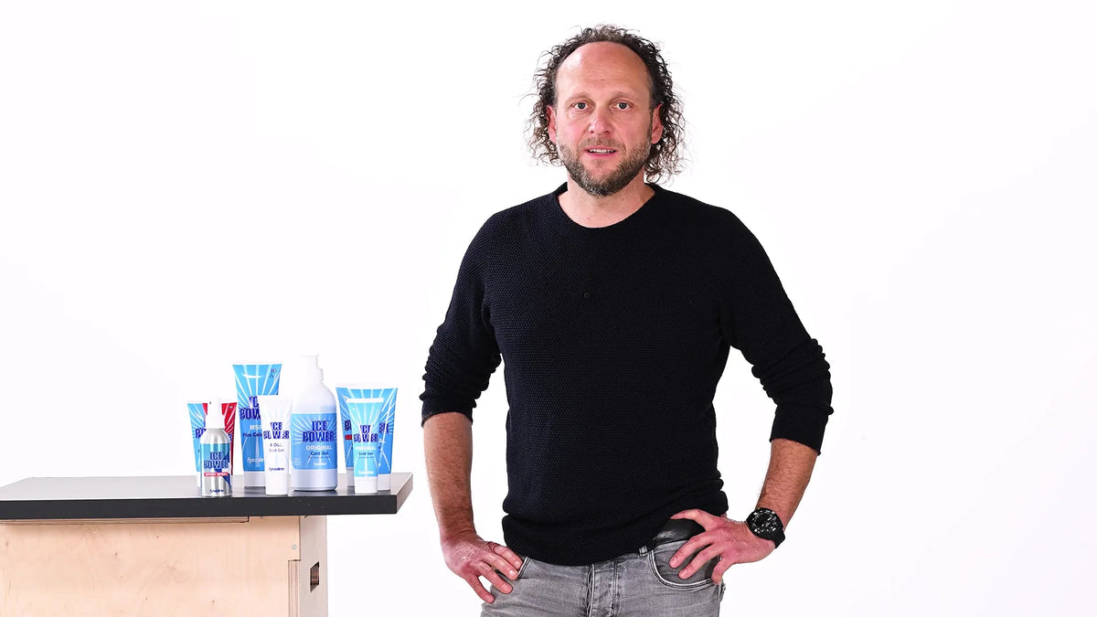 Felix Artzt vor weißem Hintergrund mit verschiedenen Biofreeze Kühlgels auf einem Tisch neben ihm.