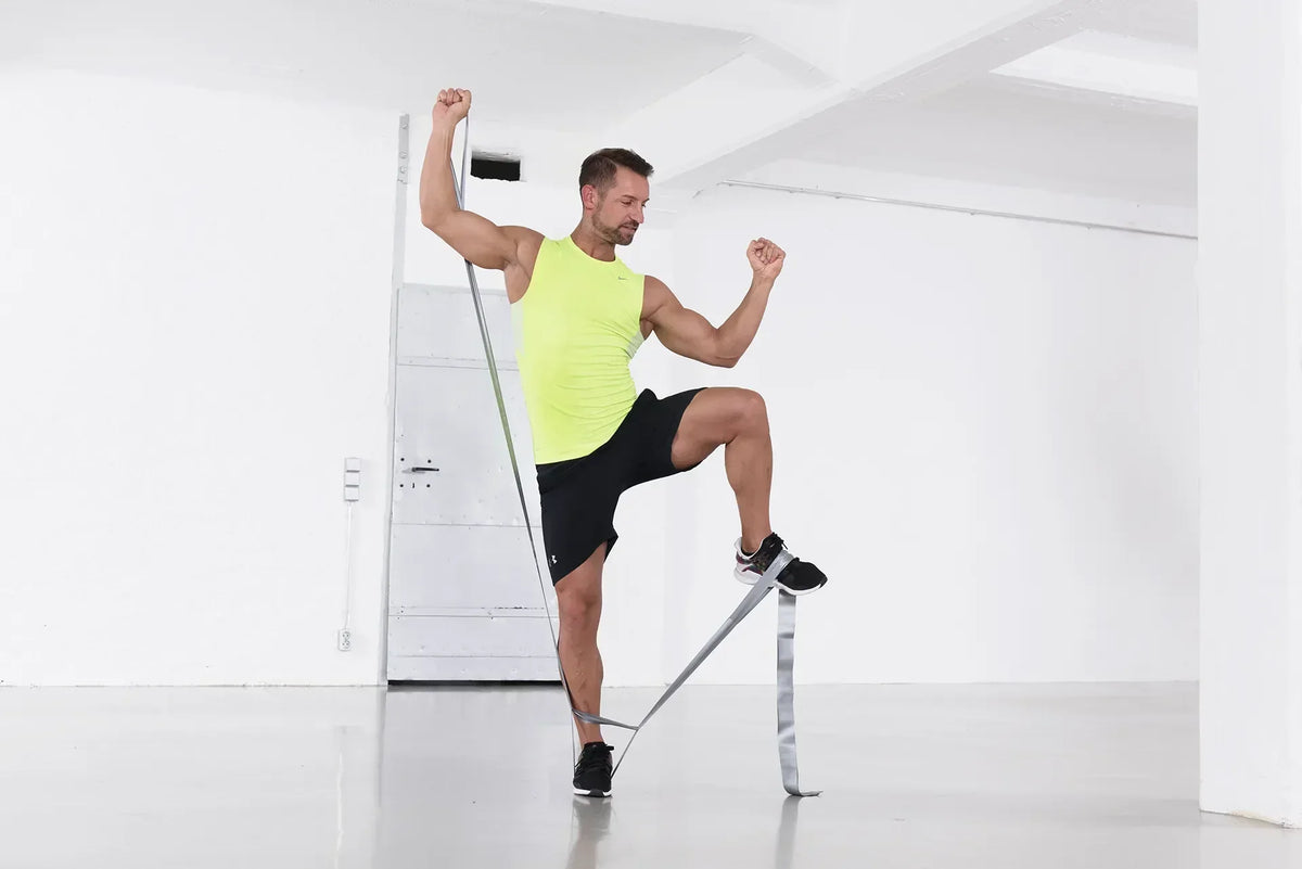 Mann führt ein Workout im Home Gym mit dem TheraBand CLX durch, steht einbeinig und nutzt das Widerstandsband für eine Kraftübung in einem hellen Trainingsraum.