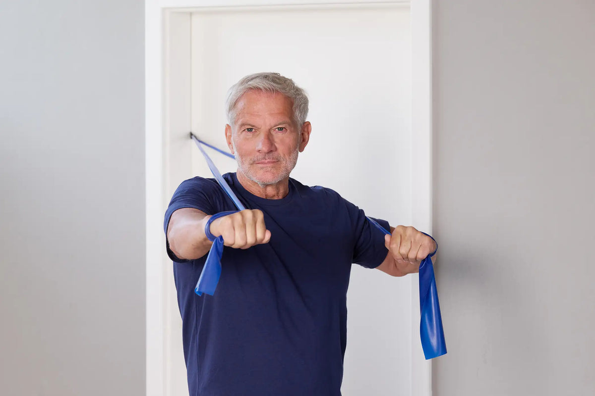 Mann trainiert mit einem blauen TheraBand mit Türanker