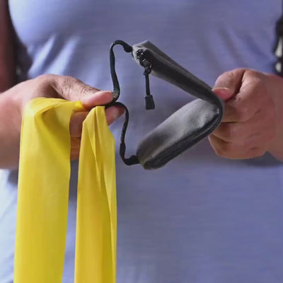 Video in Nahaufnahme, das zeigt, wie ein gelbes TheraBand in 2,50 m Länge durch an der beiliegenden Türanker-Tasche befestigt wird, welche anschließend in eine weiße Tür geklemmt wird.