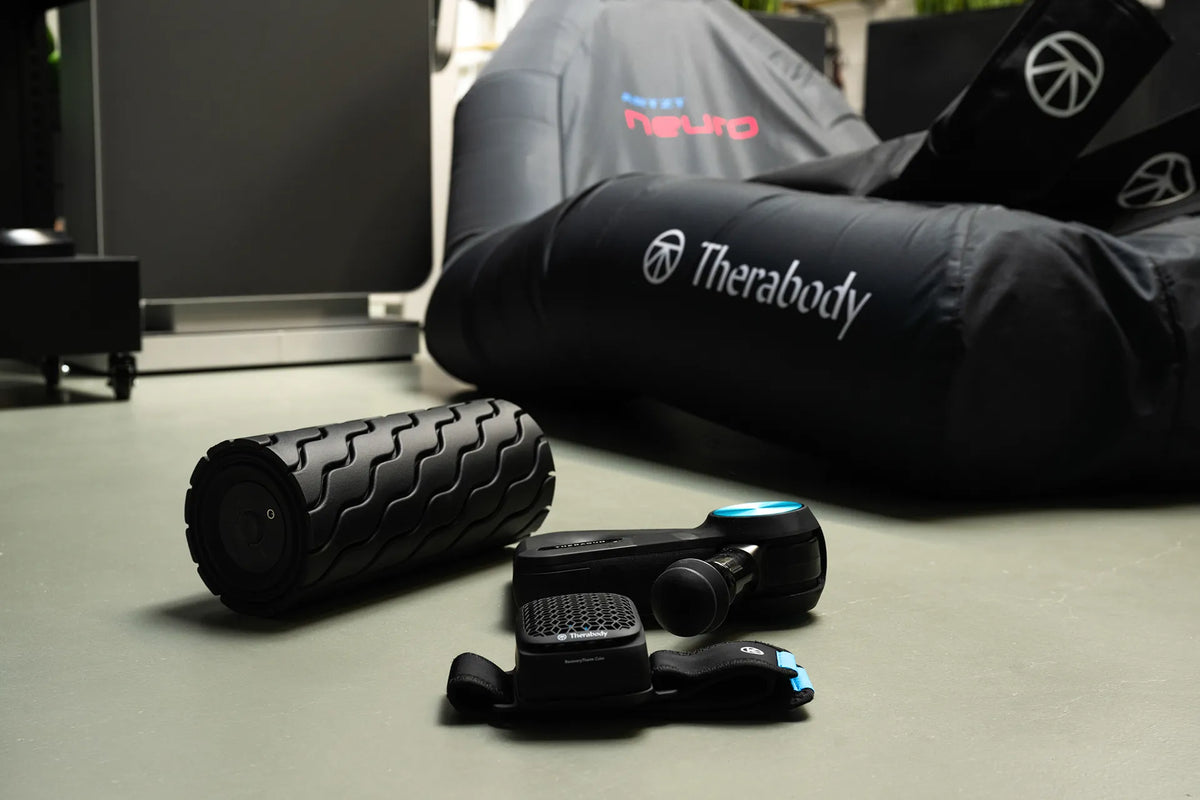 Faszienrolle, RecoveryCube und Theragun der Marke Therabody liegen auf einem grauen Boden.